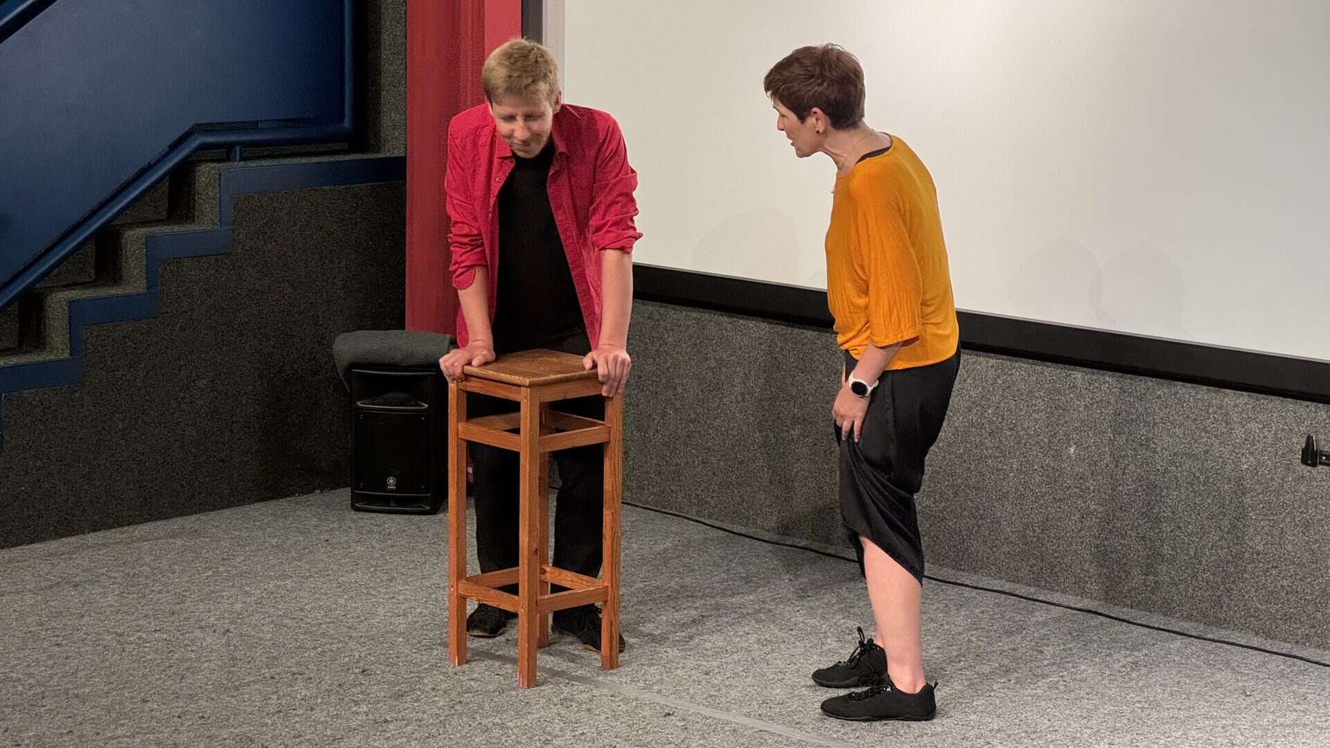 Zwei Personen bei Theaterprobe mit Hocker.