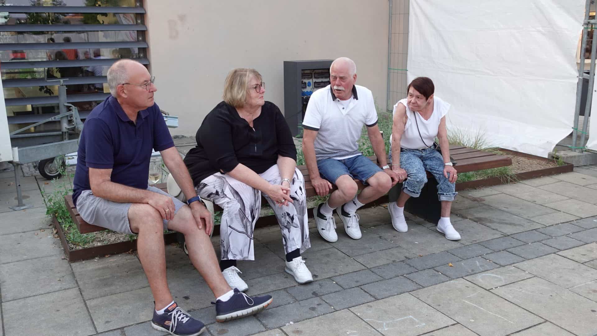 Vier Personen sitzen auf einer Bank draußen.