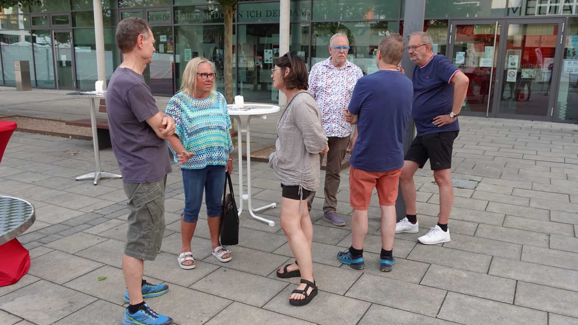 Gruppe von Menschen unterhält sich draußen vor einem Gebäude.