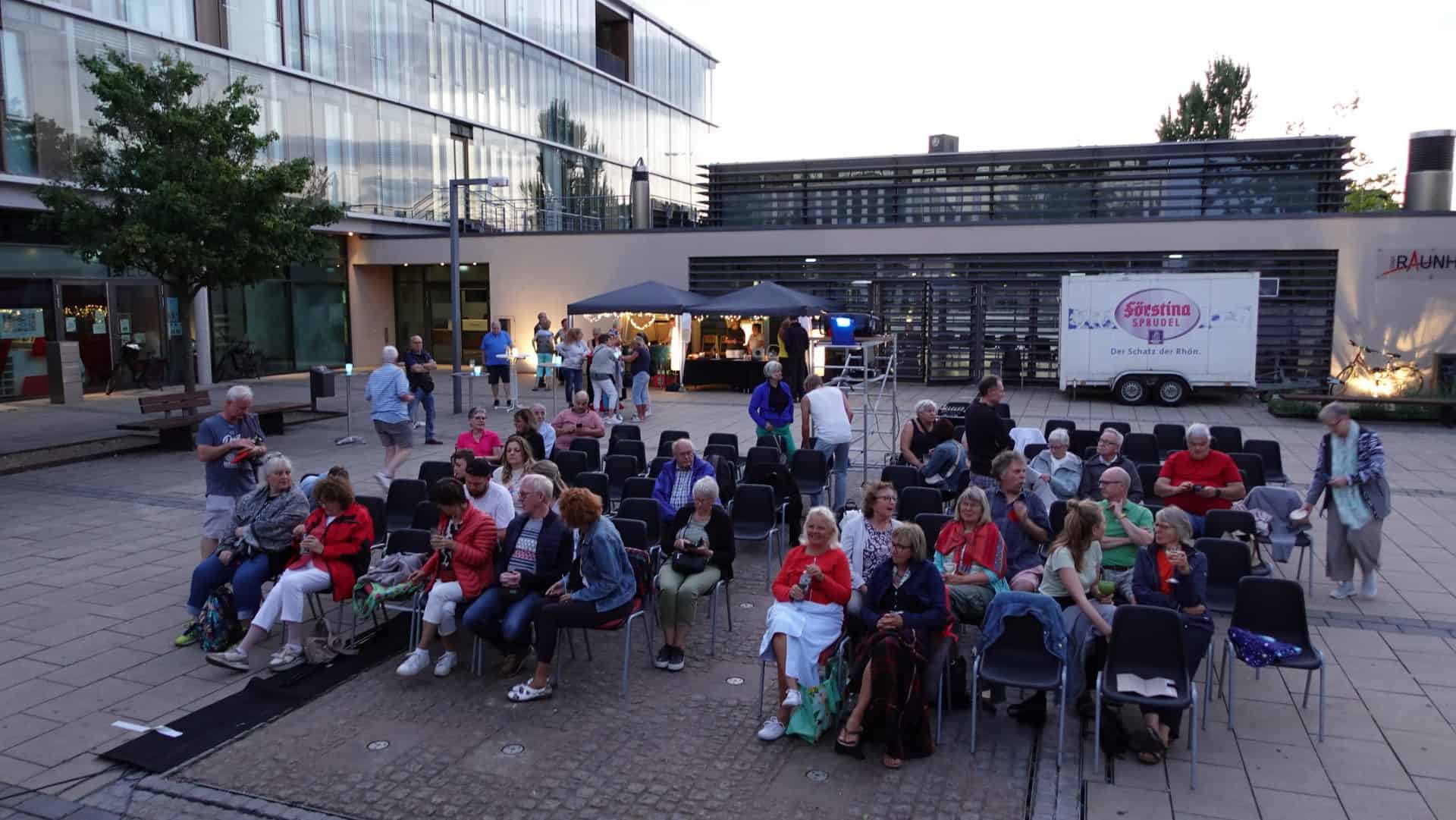 Menschen sitzen auf Stühlen vor einem Veranstaltungszelt.