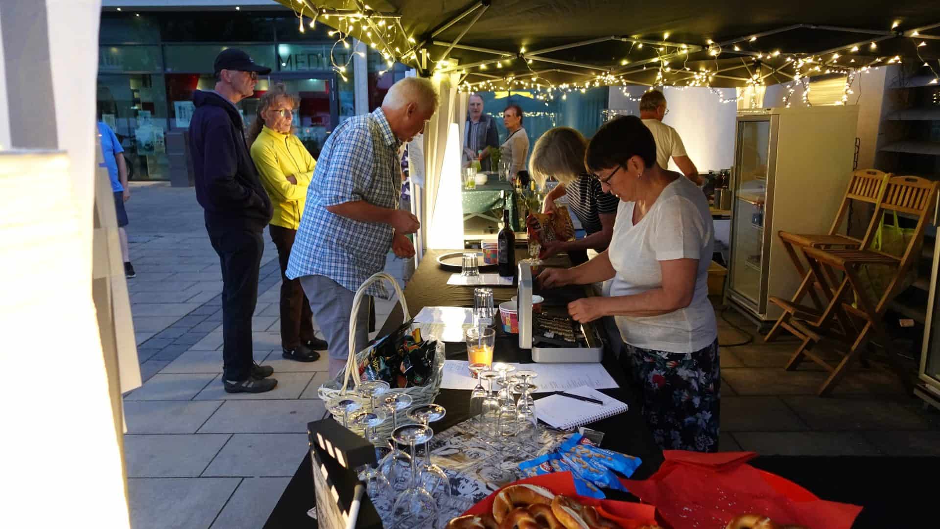 Menschen genießen Snacks an einem beleuchteten Marktstand.