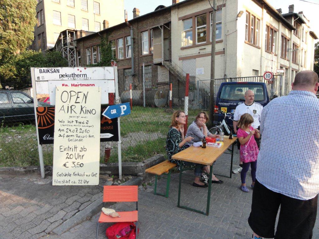 Open Air Kino mit Schild und Menschen am Tisch.