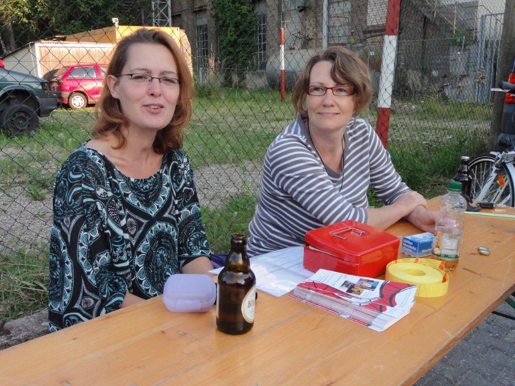 Zwei Frauen sitzen an einem Holztisch im Freien.
