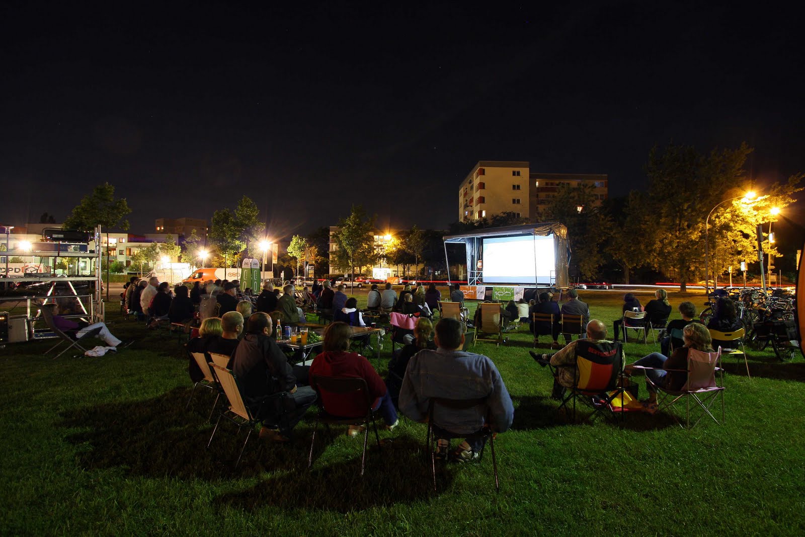 Menschen im Freien bei Nacht, schauen auf eine Leinwand.