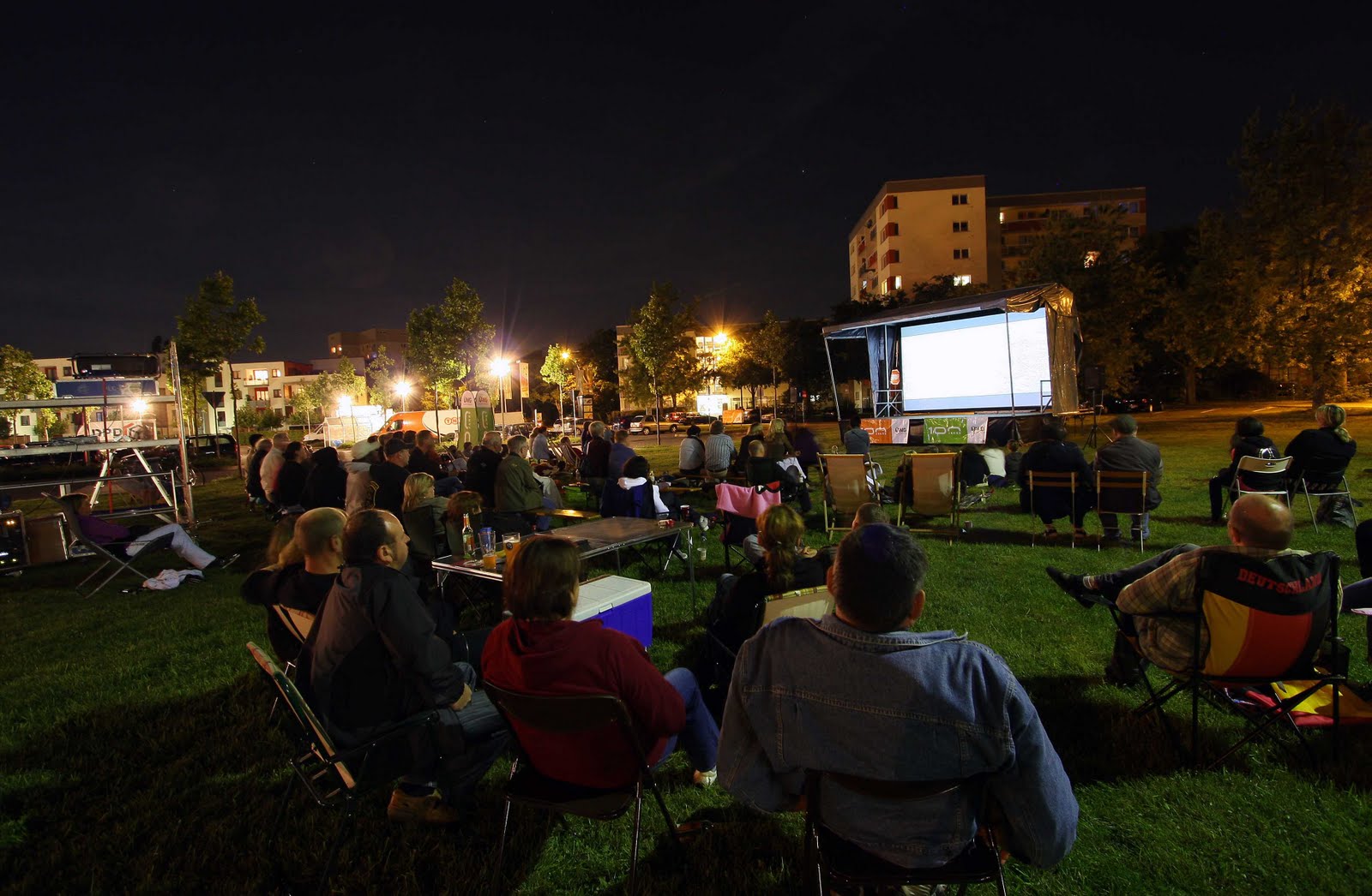 Menschen schauen Film auf Leinwand im Freien nachts.
