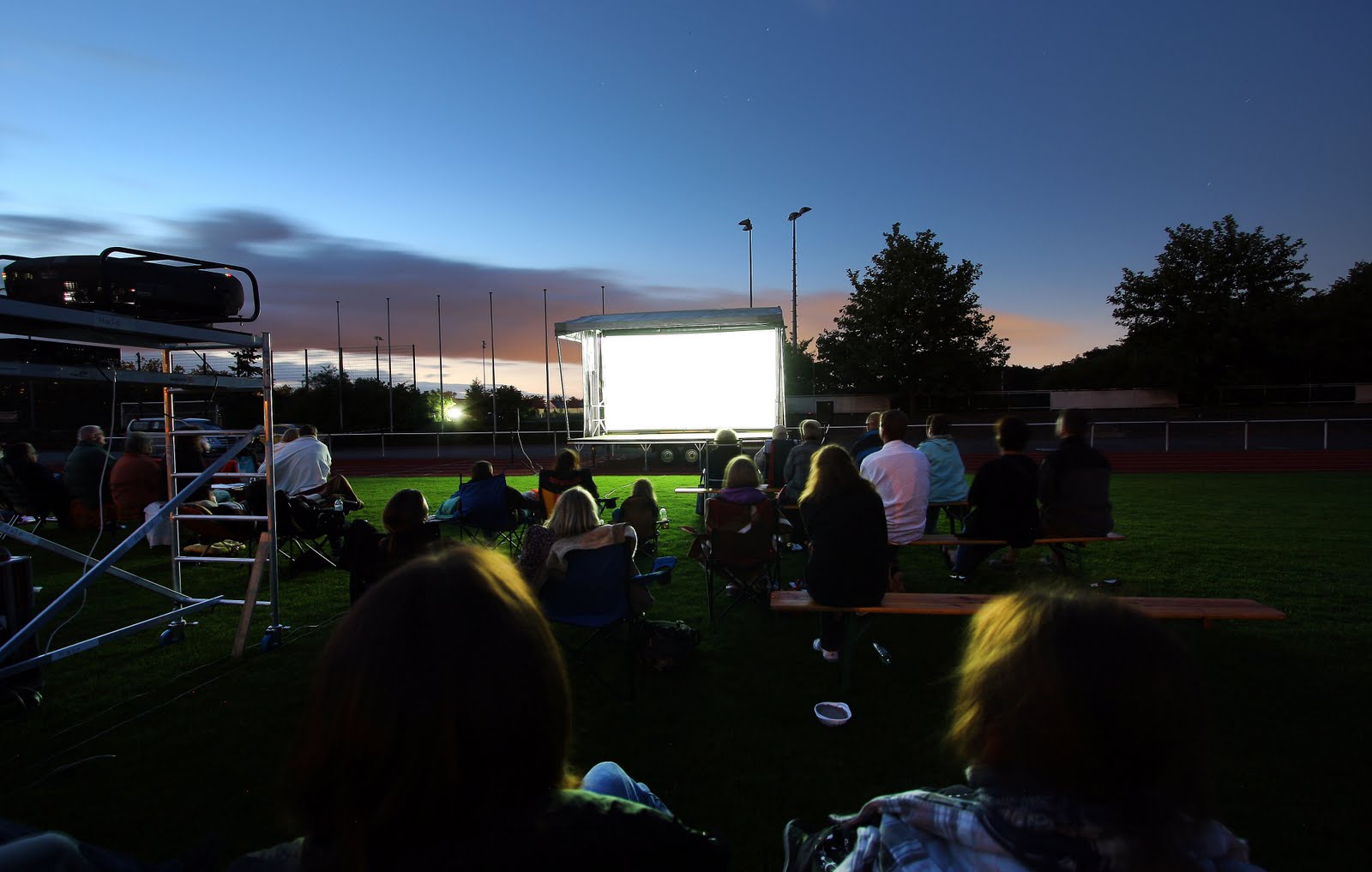 Menschen schauen einen Outdoor-Film bei Abenddämmerung.