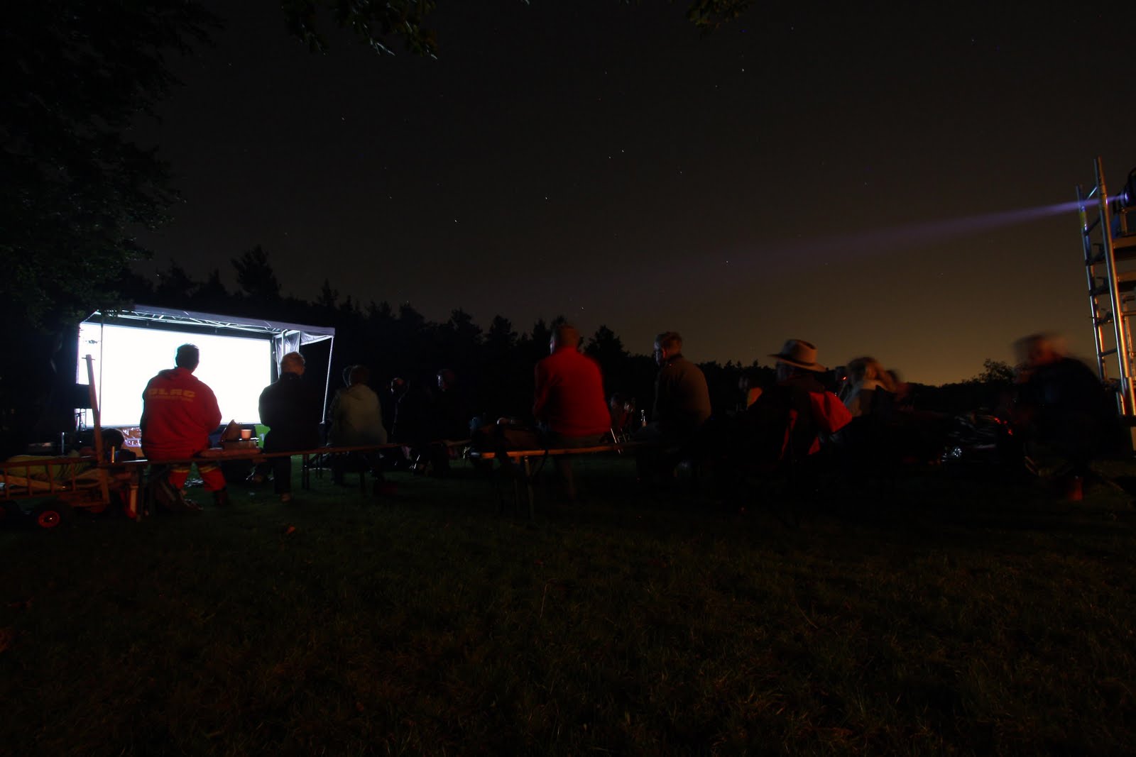 Menschen schauen bei Nacht im Freien einen Film.