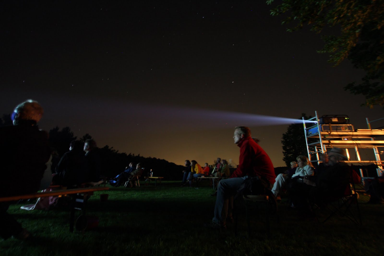 Menschen im Freien bei Nacht schauen einen Film.