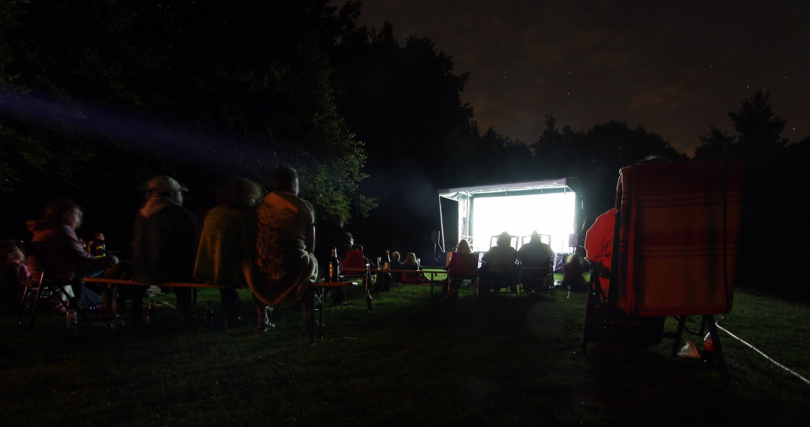Menschen schauen bei Nacht einen Film im Freien.