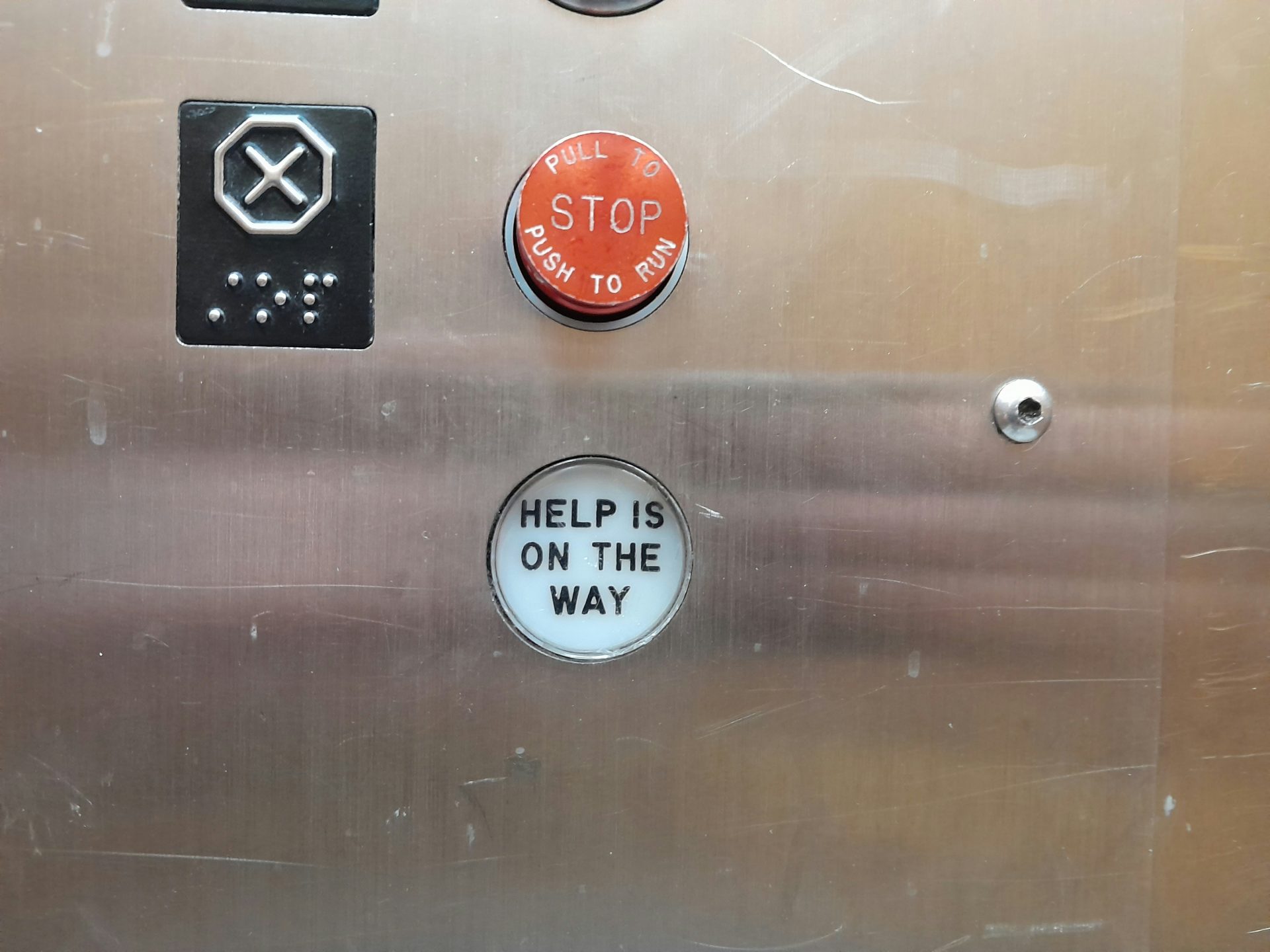 Aufzug-Notfallknopf mit Braille-Schrift und Hinweistext.