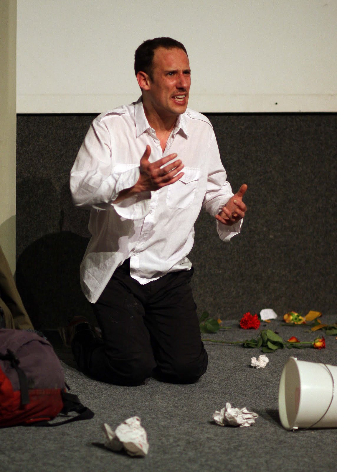 Mann kniet auf Bühne mit zerknülltem Papier und Blumen.