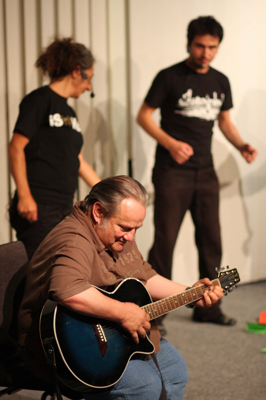 Mann spielt Gitarre, zwei Personen im Hintergrund